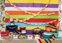 a table topped with lots of food next to a colorful wall covered in tassels