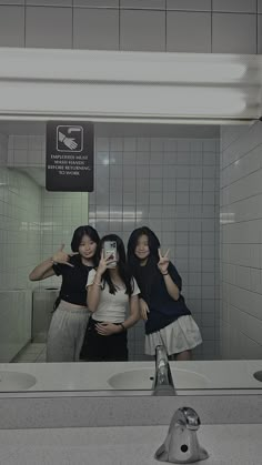 two women taking a selfie in a bathroom mirror with the reflection of another woman