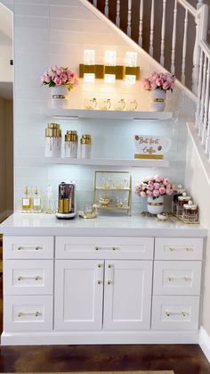 a white kitchen with gold accents and pink flowers on the counter top next to stairs