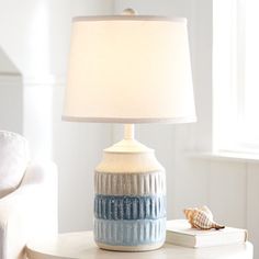 a table with a lamp on top of it next to a book and a chair