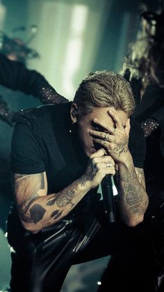 a man with tattoos holding his hands to his face as he sings into a microphone