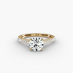 a yellow gold engagement ring with diamonds on the band and a round brilliant center stone