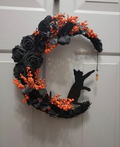 a black cat sitting on top of a door next to a wreath with orange flowers