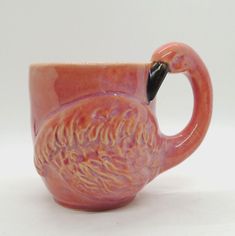 a pink flamingo shaped mug sitting on top of a white table