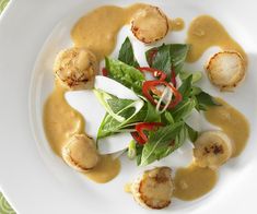 a white plate topped with scallops covered in sauce and garnished with green leaves