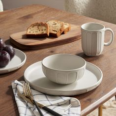 a table topped with plates and bowls filled with fruit next to bread on top of a cutting board