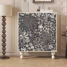 a white cabinet with black and white flowers on it in a living room next to a lamp