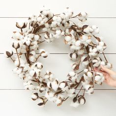 a wreath made out of cotton is being held by someone's hand over a white wooden background