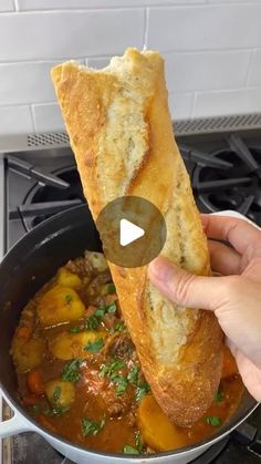 someone is holding up a piece of bread over a pot of stew