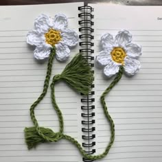 two crocheted flowers sitting on top of an open spiral notebook with string attached to them