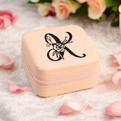 a small pink box with a monogrammed initial on the side and flowers in the background