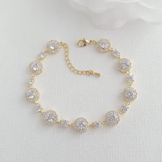 a gold bracelet with crystal stones on it and a white rose in the back ground