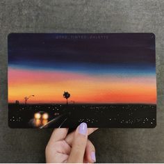 a person holding up a card that has a sunset on it and palm trees in the background