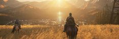 two people riding horses through a field with mountains in the background