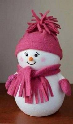 a white snowman wearing a pink hat and scarf on top of a wooden table