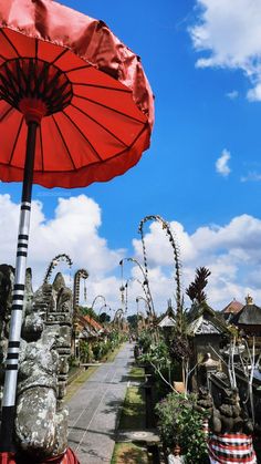 a red umbrella sitting on the side of a road in front of some statues and trees