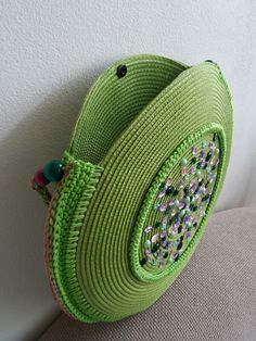 a green purse sitting on top of a couch next to a white wall with beads