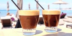 two drinks sitting on top of a wooden table next to each other in front of the ocean