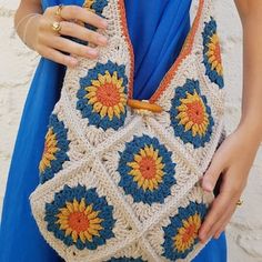 a woman wearing a blue dress holding a crocheted purse with sunflowers on it