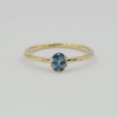 a yellow gold ring with a blue topazte stone in the center, sitting on a white surface