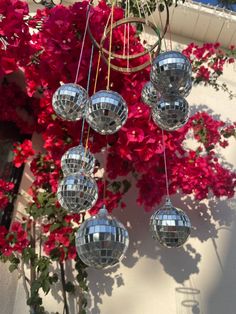 a bunch of disco balls hanging from the side of a building with red flowers behind them