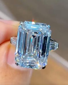 a close up of a person holding a ring with an emerald and baguette cut diamond