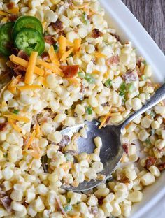 a white bowl filled with corn, cheese and jalapenos next to a spoon