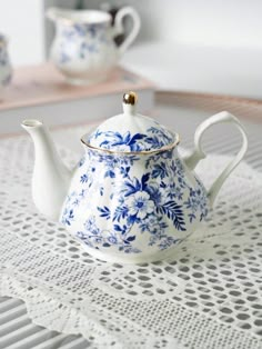 a blue and white tea pot sitting on top of a lace doily table cloth