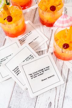 three cocktails with pineapple and cherries in them on a white wooden table