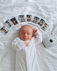 a baby laying on top of a white bed next to polaroid pictures and a camera