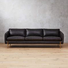 a black leather couch sitting on top of a hard wood floor next to a gray wall