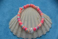 a pink and blue beaded bracelet sitting on top of a seashell with a shell