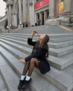 a woman is sitting on the steps drinking from a bottle in front of a building