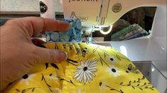 someone is using a sewing machine to sew on a yellow flowered dress with black and white flowers