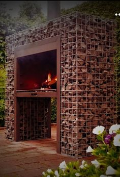 an outdoor fireplace made out of bricks in the middle of some bushes and flowers around it