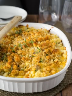 a casserole dish with cheese and herbs in it on a wooden table next to wine glasses