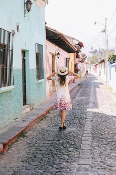 a woman in a hat walking down a cobblestone road with her arms behind her head