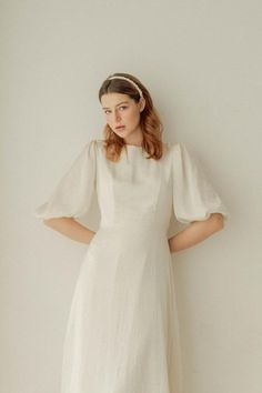 a woman standing in front of a wall wearing a white dress with puffy sleeves