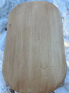 a wooden cutting board sitting on top of a white tablecloth covered floor with plastic wrap around it