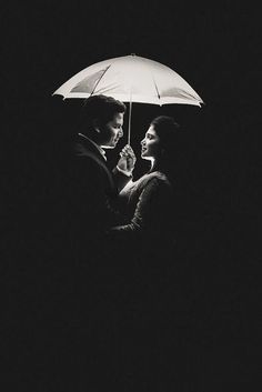 a man and woman standing under an umbrella in the dark with their faces close to each other