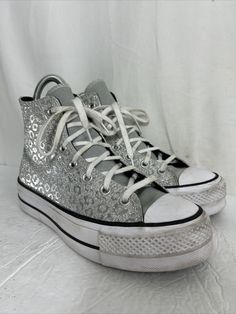 Elevate your style with these stunning Converse Chuck Taylor All Star Platform High sneakers. The unique design showcases glitter leopard spots on a silver background, making them a statement piece in any outfit. The high top shoe shaft style provides comfort and support, while the durable athletic material ensures long-lasting wear. These sneakers feature a US shoe size of 8 and a style code of 572043C. The Converse brand is renowned for its quality and style, making these shoes a must-have for Trendy Metallic High-top Sneakers, Silver Sneakers For Streetwear With Speckled Midsole, Silver Sneakers With Speckled Midsole For Streetwear, Metallic Sneakers With Speckled Midsole For Streetwear, Silver Low-top Platform Sneakers, Casual Silver High-top Lace-up Sneakers, Silver High-top Sneakers With Speckled Midsole, Metallic High-top Sneakers With Speckled Midsole, Casual Silver High-top Sneakers With Speckled Midsole