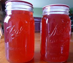 two jars filled with red liquid sitting on top of a wooden table