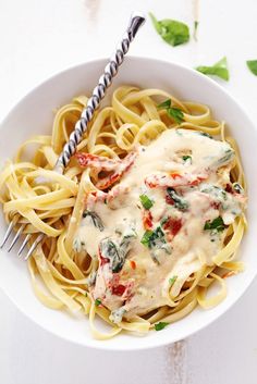 a white bowl filled with pasta covered in sauce and spinach sprinkled on top