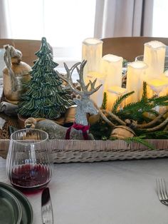 a tray with candles and christmas decorations on top of a table next to a glass of wine