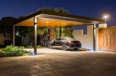 a car is parked in the driveway under a pergolated structure at night with lights on