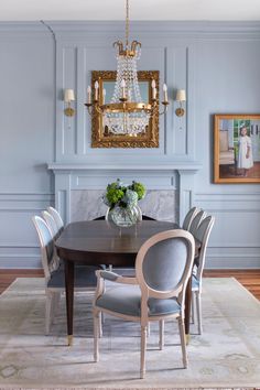 a dining room table with chairs and a chandelier hanging above it in front of a fireplace