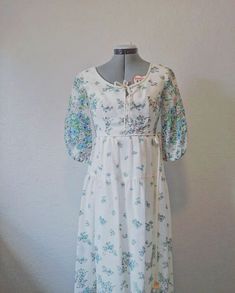 "This is a gorgeous and super nostalgic Designer Spring/Summer Dress by House of Bianchi of Boston. Tags are present. Two tiny frays at the hem of the shear outer floral lining.  Flouncy sheer half sleeves and an empire waste with a scoop neckline make this a dreamy party dress one for the books. This beauty is complete with a plastic zipper with white painted metal Talon zipper head. Long waist ties hang from the right side for cinching and adding that extra bow. The scoop neckline has a decorative tiny v that is secured in the front with a tie for a bow.  *This garment has been hand steamed* Measurements: Length- 56\" Shoulders- 15\" Sleeves- 22\" Bust- 34\" Waist- 30\" Hip- 36\"" Bohemian Prairie Dress With Floral Print For Garden Party, Bohemian Prairie Dress For Summer Garden Party, Summer Bohemian Prairie Dress For Garden Party, Spring Peasant Prairie Dress With Floral Print, Spring Peasant Style Prairie Dress With Floral Print, Spring Floral Print Peasant Prairie Dress, Spring Floral Print Prairie Peasant Dress, Bohemian Fitted Prairie Dress With Floral Print, Bohemian Midi Prairie Dress For Spring