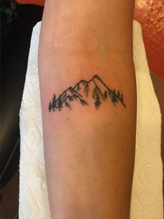 a tattoo on the arm of a woman with mountains and pine trees in the background