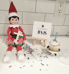 an elf is sitting next to a cupcake and a sign that says happy birthday jesus