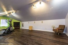 an empty room with hard wood flooring and a chair in the corner next to a treadmill